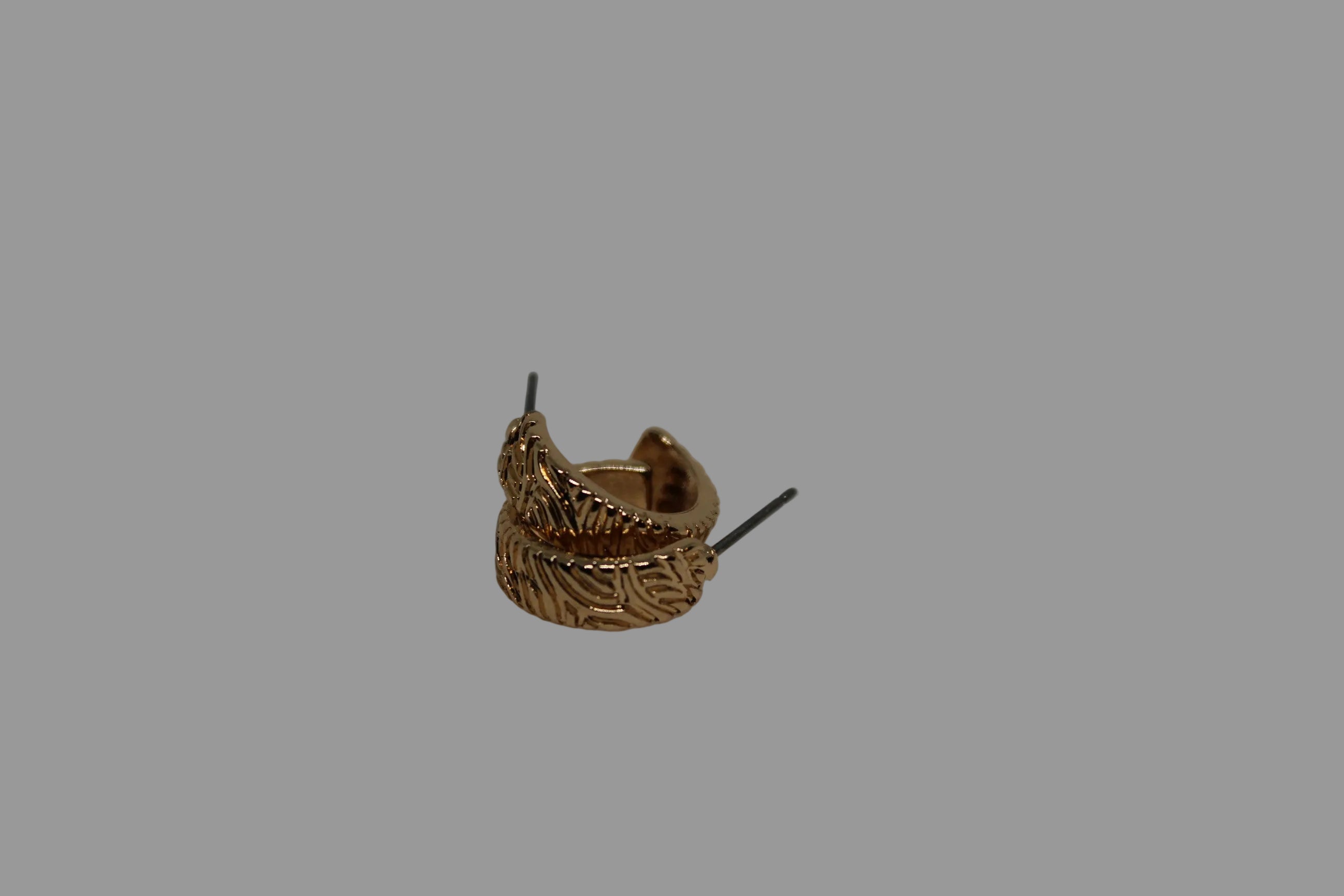 A small gold huggie hoop earring with a textured, leaf-like or feather-like embossed pattern, shown on a plain light gray background.