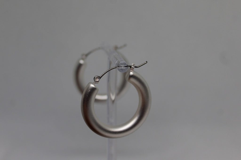 A pair of thick, polished silver hoop earrings displayed on a clear plastic stand against a neutral gray background.
