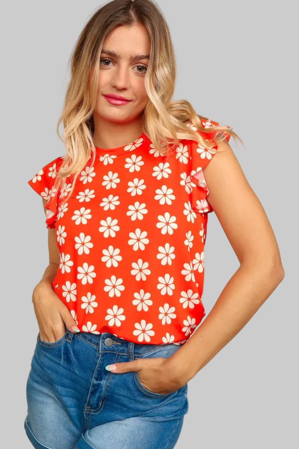 Woman wearing a red top with white floral pattern and blue jeans on a beige background