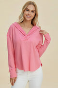 Woman wearing a pink long-sleeve top with a hood against a beige background