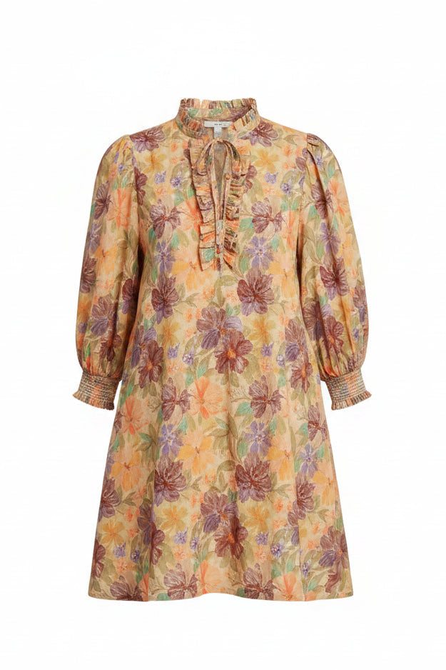 A woman modeling a long-sleeve, knee-length floral shirt dress with a button-up front, ruffled collar, and voluminous sleeves, paired with black ankle boots against a solid gray studio background.